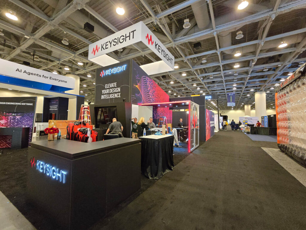 32 Creative Trade Show Booth Ideas To Attract Visitors And Leads In 2025 8 The large and prominent keysight exhibition booth at the ai engineer world's fair, featuring multiple hanging signs, interactive displays with "elevate your design intelligence" messaging, and a modern, angular design in black and red.