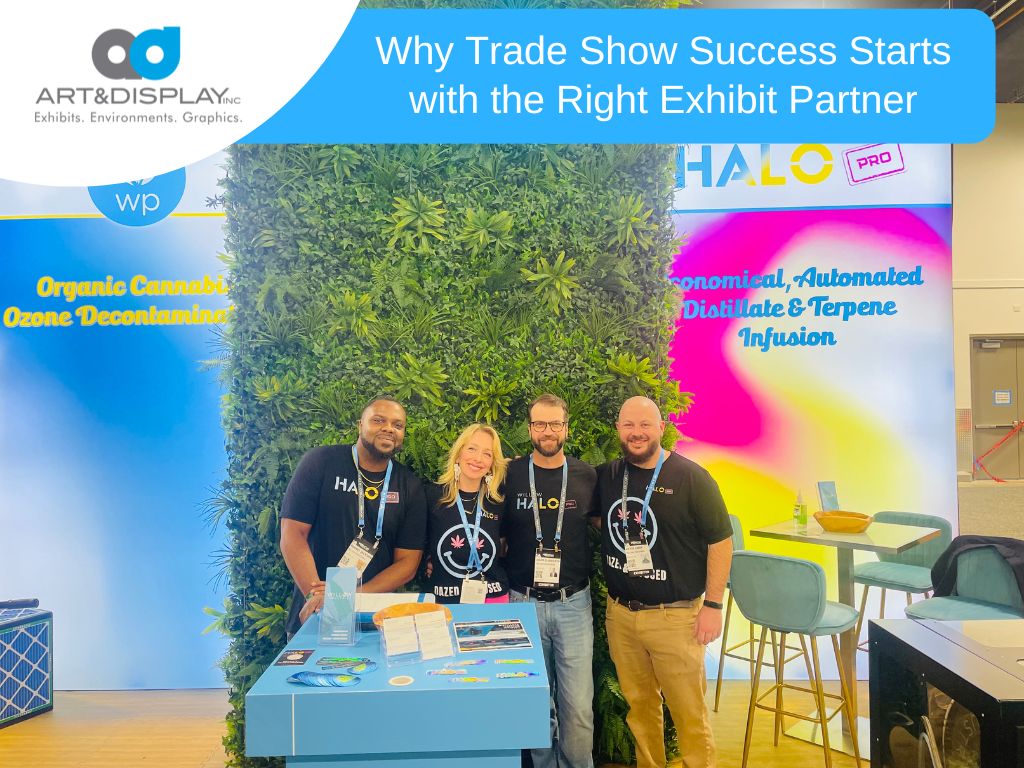 Trade show team standing at a custom exhibit booth with branded graphics and a green wall backdrop, highlighting partnership-driven exhibit design.