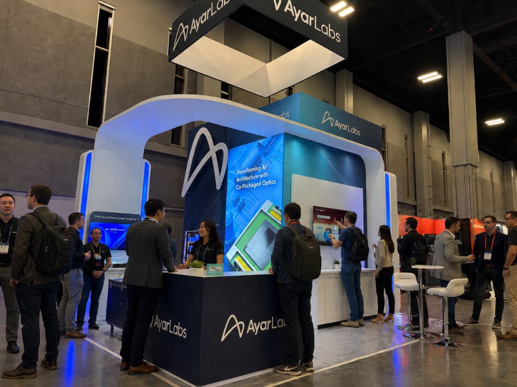 Modern trade show booth design by ayar labs with led displays, branded signage, and attendees engaging at an exhibition booth