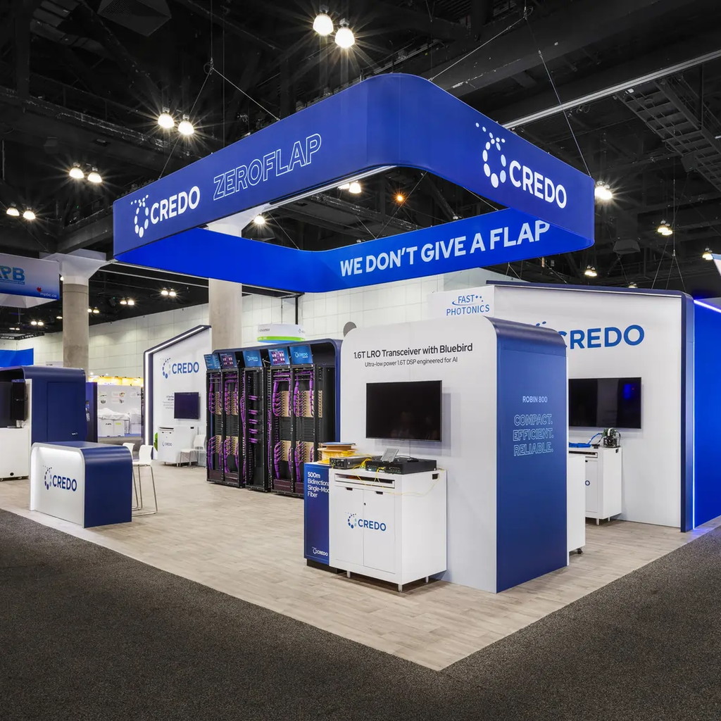 Credo trade show booth with a large blue suspended header sign, server rack display, and white product demo counters