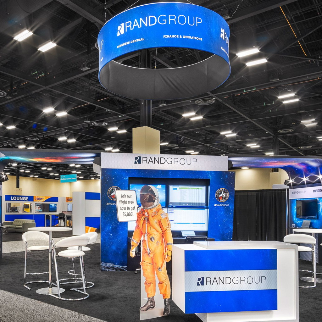 Rand group island trade show booth with blue circular hanging sign, space-themed graphics, and astronaut cutout at the entrance
