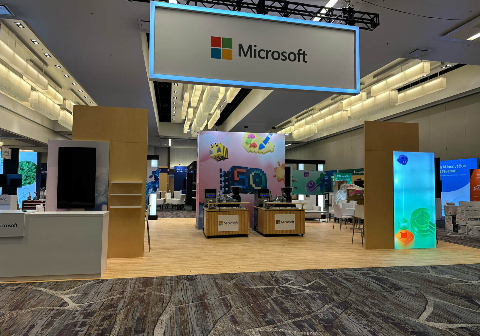 The microsoft exhibition booth at the ai engineer world's fair, featuring a large overhead illuminated sign, interactive display stations, colorful graphics, and a spacious layout with wooden flooring.