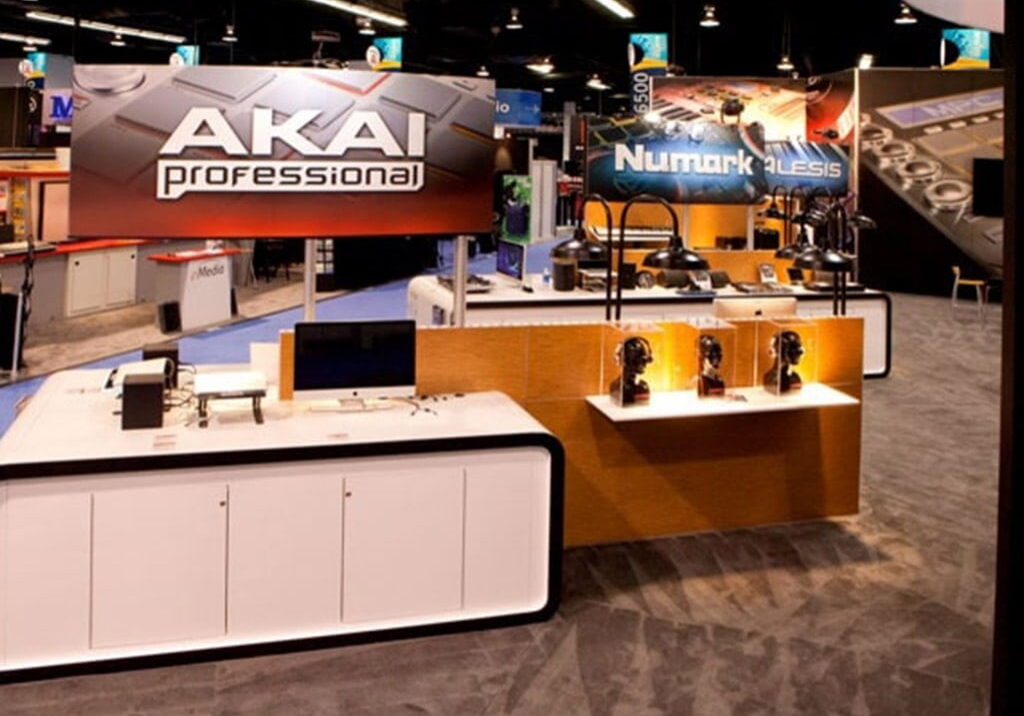 Akai professional and numark trade show booth with backlit overhead signage, white gloss product counters, and wood display pedestals
